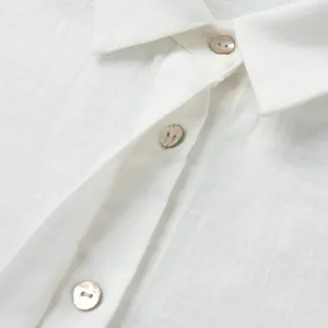 Détail rapproché d'une chemise en lin blanc avec des boutons en nacre irisée sur le col