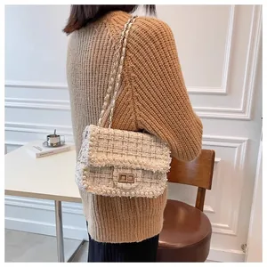 Close-up view of the elegant white pearl-embellished tweed bag styled with a brown sweater