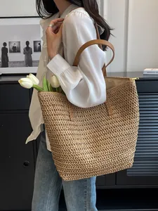 Large woven straw tote bag with brown straps styled with white tulips for summer.