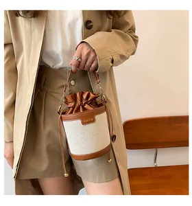 Detail shot of a niche canvas and leather bucket bag held by a model in a trench coat