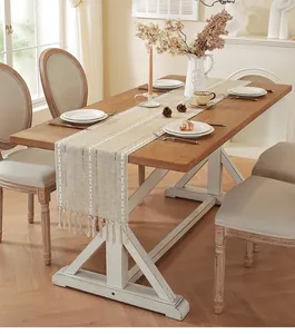 Rustic cream cotton linen table runner with white embroidery and tassels on a wooden table