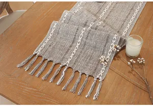 Close-up of linen table runner with handmade tassels and white embroidery on a wooden table