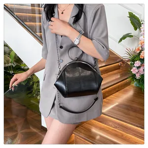 Sac coquille noir chic avec poignée ronde et bandoulière chaîne porté par un modèle.
