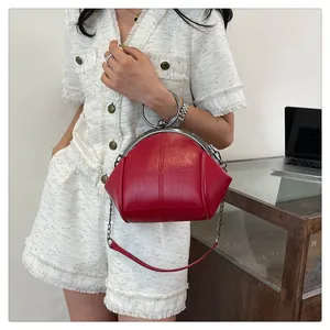 Détail d'un sac rouge en forme de coquillage avec poignée métallique porté par un mannequin.
