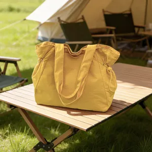 Große gelbe wasserdichte Stofftragetasche auf einem hölzernen Campingplatz-Tisch im Freien