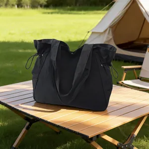 Schwarze wasserdichte Nylon-Tragetasche auf einem Camping-Holztisch im Freien präsentiert.