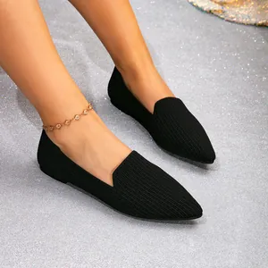 Detailed close-up of black pointed-toe knit flat shoes on a silver glitter background