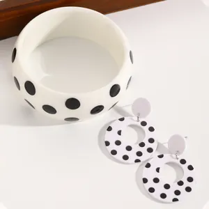 Detail view of black and white polka dot acrylic bangle and circular dangle earrings