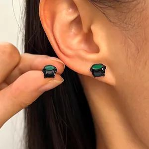 Detailed macro view of gothic Halloween cauldron stud earrings featuring green witch potion