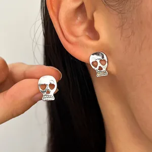 Silver gothic skull stud earrings for Halloween, shown being worn and held by hand.