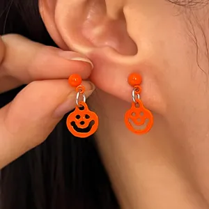 Macro detail of bright orange Halloween pumpkin smiley face drop earrings on ear