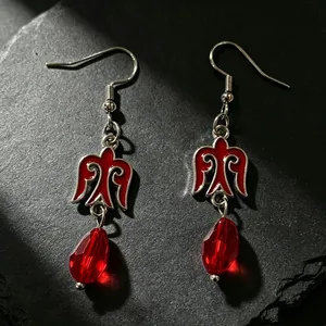 Detalle de pendientes de estilo kazajo con pájaro de esmalte rojo y cuenta facetada.