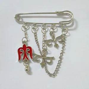Detalle de un broche de imperdible plateado de estilo kazajo con pájaro esmaltado rojo.