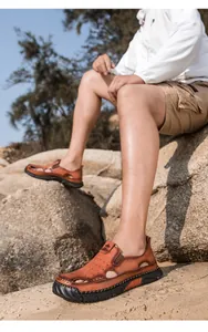 Detailopname van bruine lederen heren sandalen met gaten op een rotsachtig strand.