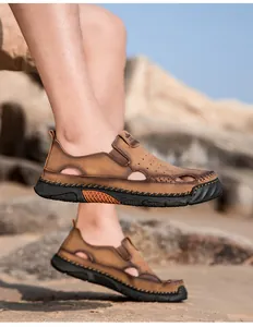 Buitenopname van bruine lederen herensandalen met gaten op een zonnig zandstrand
