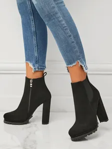 Close-up detail view of black chunky high heel ankle boots worn with frayed denim jeans