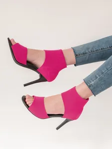 Close-up of vibrant pink fly-knit high-heeled sandals worn with casual denim jeans