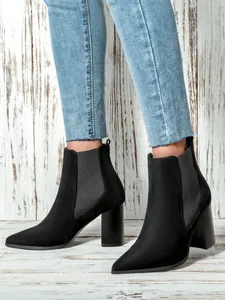 Close-up of elegant black suede ankle boots with pointed toe and chunky high heels being worn