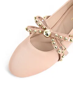 Detailed macro view of beige round-toe flat shoe featuring a stylish gold rivet bow accent