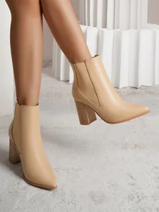 Close-up side view of elegant beige pointed toe chunky heel ankle boots on a model.