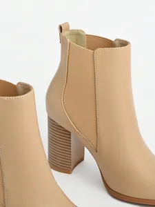 Close-up detail of women's beige chunky high heel Chelsea boots with elastic side.