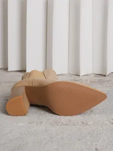 Detail view of the non-slip sole and block heel of a pointed-toe beige ankle boot.