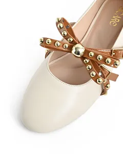 Macro view of a cream round-toe flat shoe featuring a brown studded bow buckle.