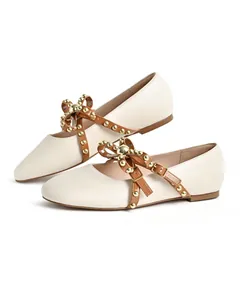 Elegant cream-colored round toe flat shoes featuring studded brown straps and decorative bows
