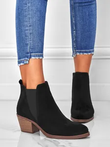 Close-up of black suede ankle boots with stacked block heel and elastic side panels.