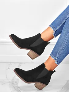 Close-up view of black suede Chelsea ankle boots with chunky wood-grain stacked heels.
