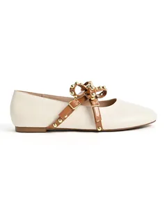 Detailed side view of beige round-toe flat shoe with studded brown strap and bow