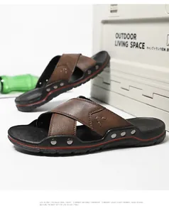 Detail van bruine leren herenslippers met kruisbanden, zachte zool en metalen studs.