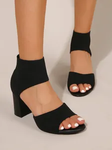 Detail view of black knit block heel sandals with open-toe design shown on feet.