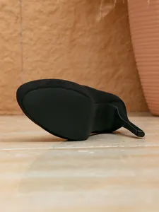 Close-up view of a black suede platform stiletto pump shoe with slip-resistant sole.
