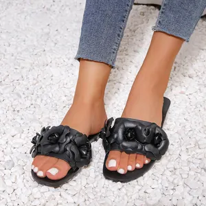 Women's black flat slide sandals with 3D floral accents on white pebble background