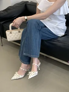 Elegant white polka dot pointed-toe stiletto mules with bow detail shown on a model