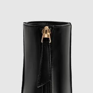 Macro detail of gold zipper and leather pull tab on black stiletto fashion boot
