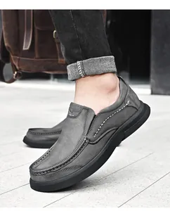Close-up van grijze leren herenloafers met decoratieve stiksels en zachte rubberen zolen.