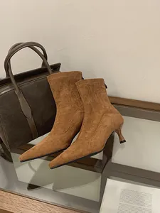Vista detallada de botines de ante marrón con elegantes tacones de aguja sobre cristal.