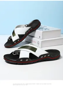 Detail van leren herensandalen met witte gekruiste banden en metalen studs.