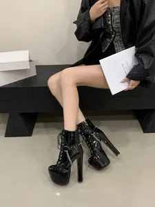 Close-up of black patent leather platform boots with metal chains and studs worn by a model