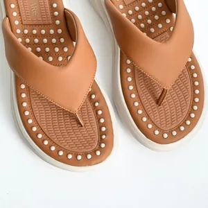 Close-up of brown thong sandals featuring a white textured massaging footbed and platform sole.