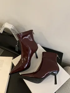Nahaufnahme von weinroten Lackleder-Stiefeletten mit spitzer Kappe auf weißem Karton.