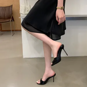 Close-up of elegant black patent leather stiletto mules with open toe design on model