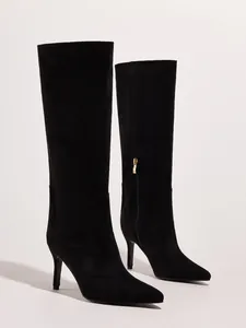 Detail view of black stiletto knee-high boots with pointed toe and gold side zipper.