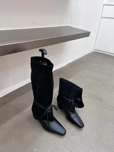 Détails de bottes noires pointues à effet plissé avec nœuds décoratifs aux chevilles.