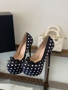 Vista detallada de elegantes tacones de aguja negros con lunares y un delicado lazo arriba