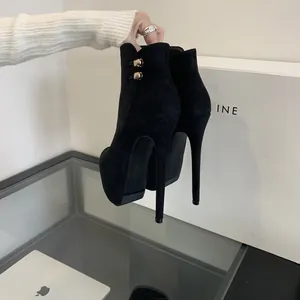 Detalle de botines de plataforma en ante negro con tacones de 16 cm y hebillas.