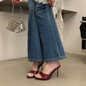 Detail shot of burgundy patent leather stiletto mules paired with wide-leg jeans.