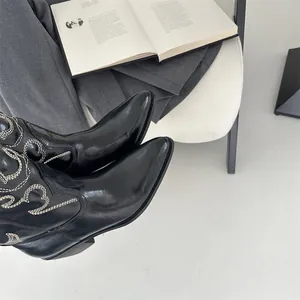 Detailansicht stylischer schwarzer Western-Cowboystiefel mit weißer Stickerei auf Stuhl